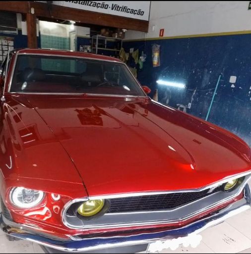 Capô vermelho de um Mustang clássico polido, refletindo as luzes da oficina