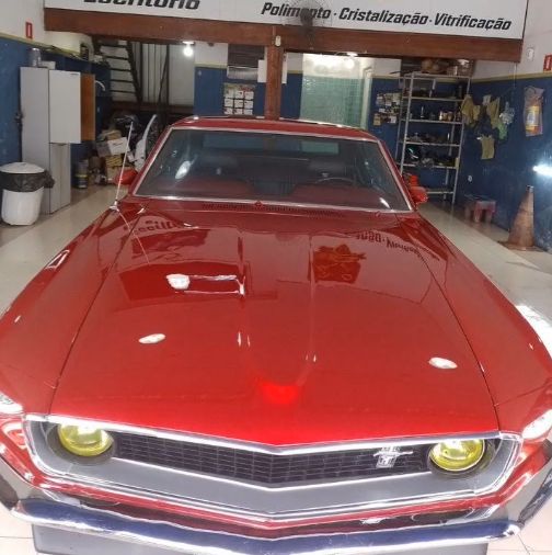 Mustang clássico vermelho visto de frente, com o capô refletindo a oficina