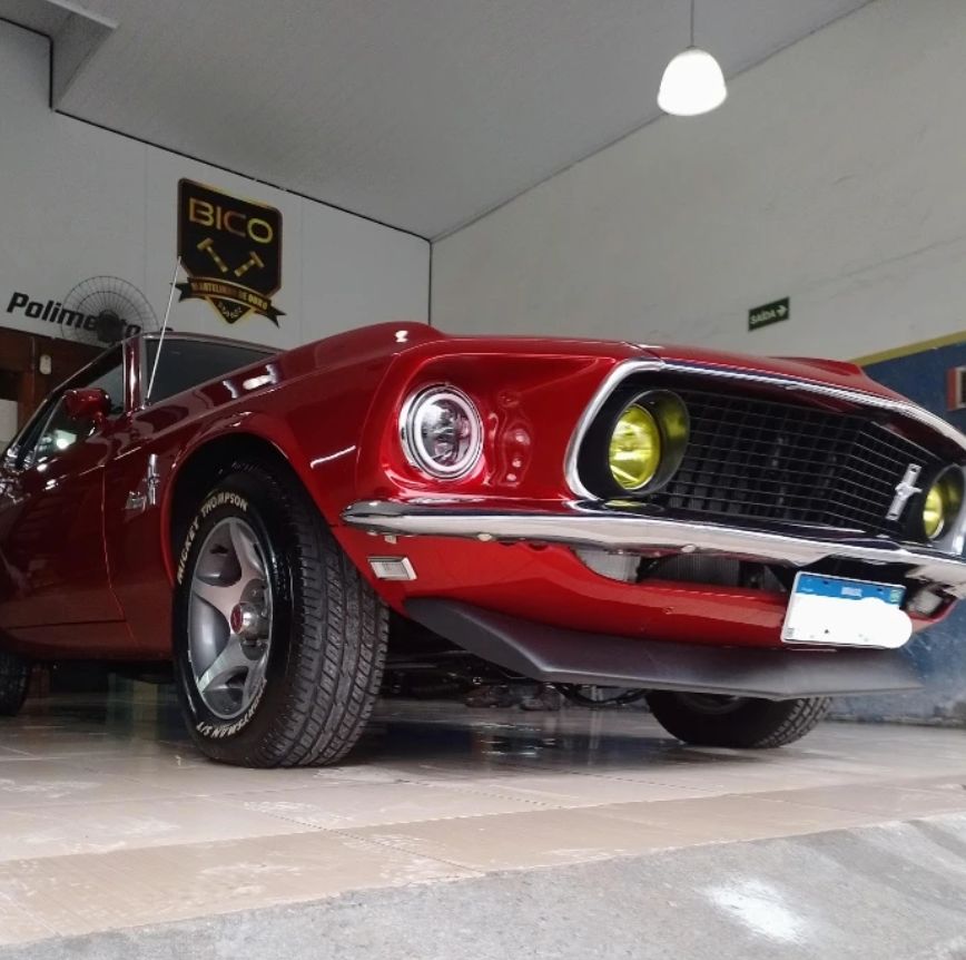 Frente de um Mustang clássico vermelho, com faróis de milha amarelos, na oficina