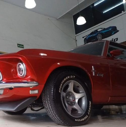 Lateral de um Mustang clássico vermelho com a pintura brilhando na oficina