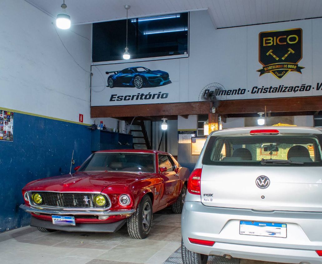 Interior da oficina com um Mustang vermelho e um Volkswagen Fox prata lado a lado
