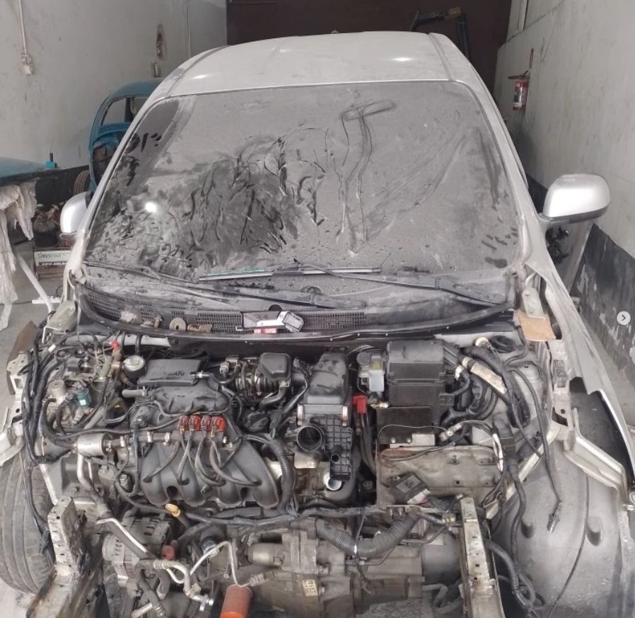 Nissan Versa prata com a frente destruída: sem para-choque, faróis e capô, com o motor à mostra